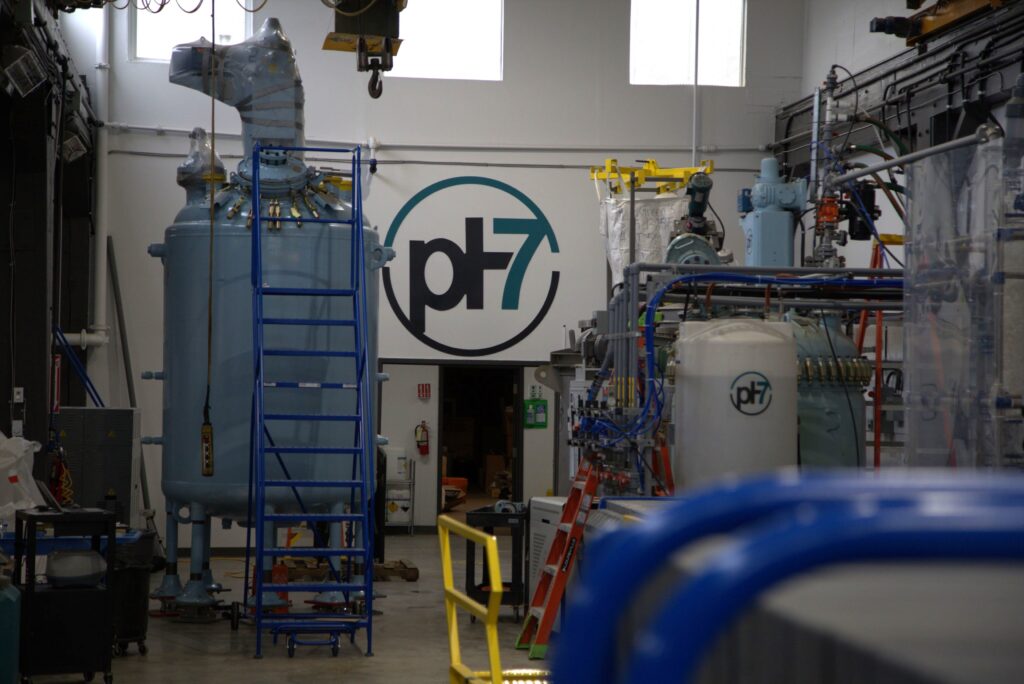 The interior of the new pH7 Technologies precious metals extraction plant. A blue tank, machinery, and pipelines, all branded with the "pH7" logo are visible.
