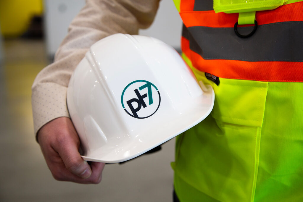 Close-up of a PH7 Technologies logo on a white safety helmet held by a worker.